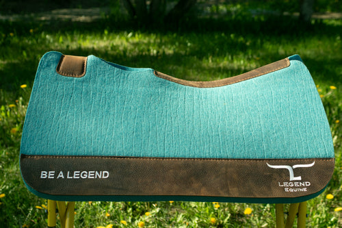Turquoise and brown wear leathers saddle pad with 'Be a Legend' branding on grass